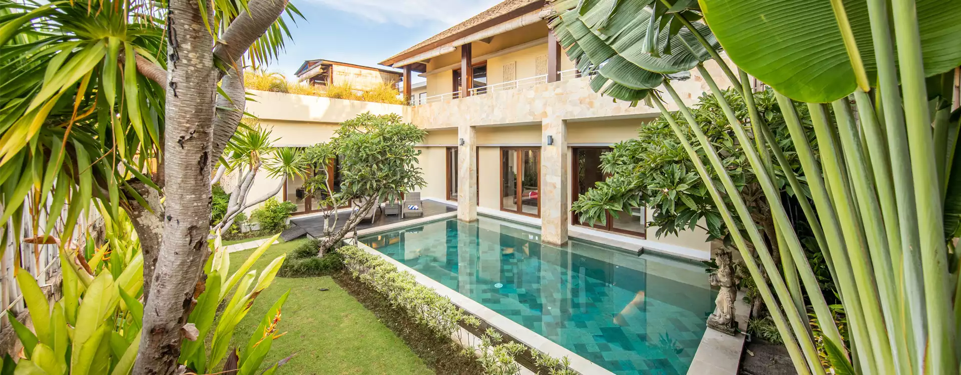 Ferienhaus Pool in Naturstein an Rollrasen, Palmen und Sträuchern