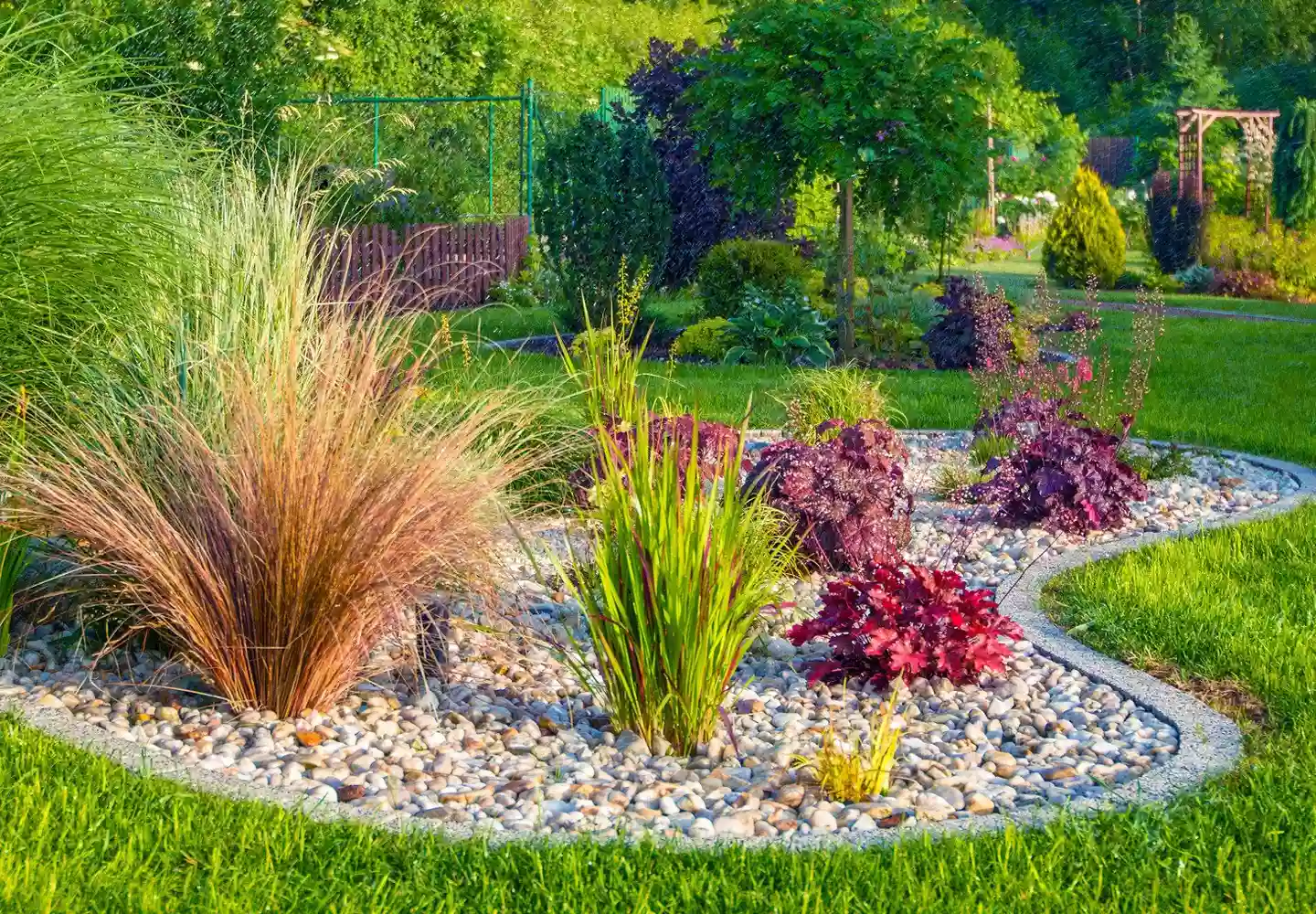 Garten- und Landschaftsgestaltung mit weitflächiger grüner Wiese, Bäumen, Sträuchern und einem Pflanzbogen. Rollrasen und Kieselemente.