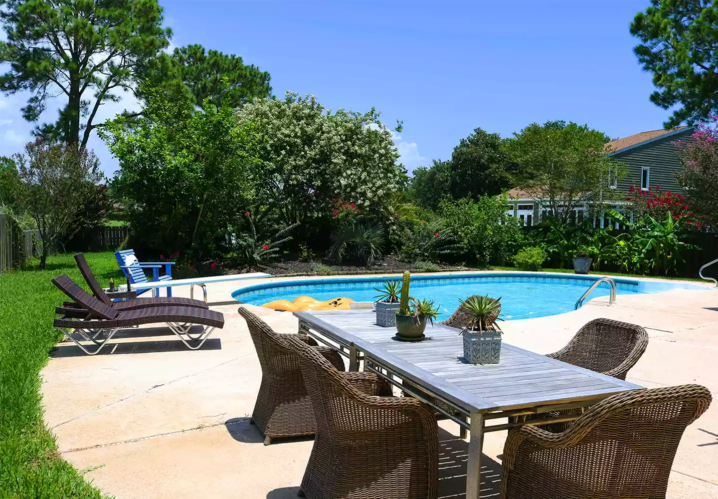 Pool im Garten an Steinterrasse mit Rattanmöbeln - im Hintergrund Rollrasen mit Bäumen und Sträuchern als Heckenbepflanzung